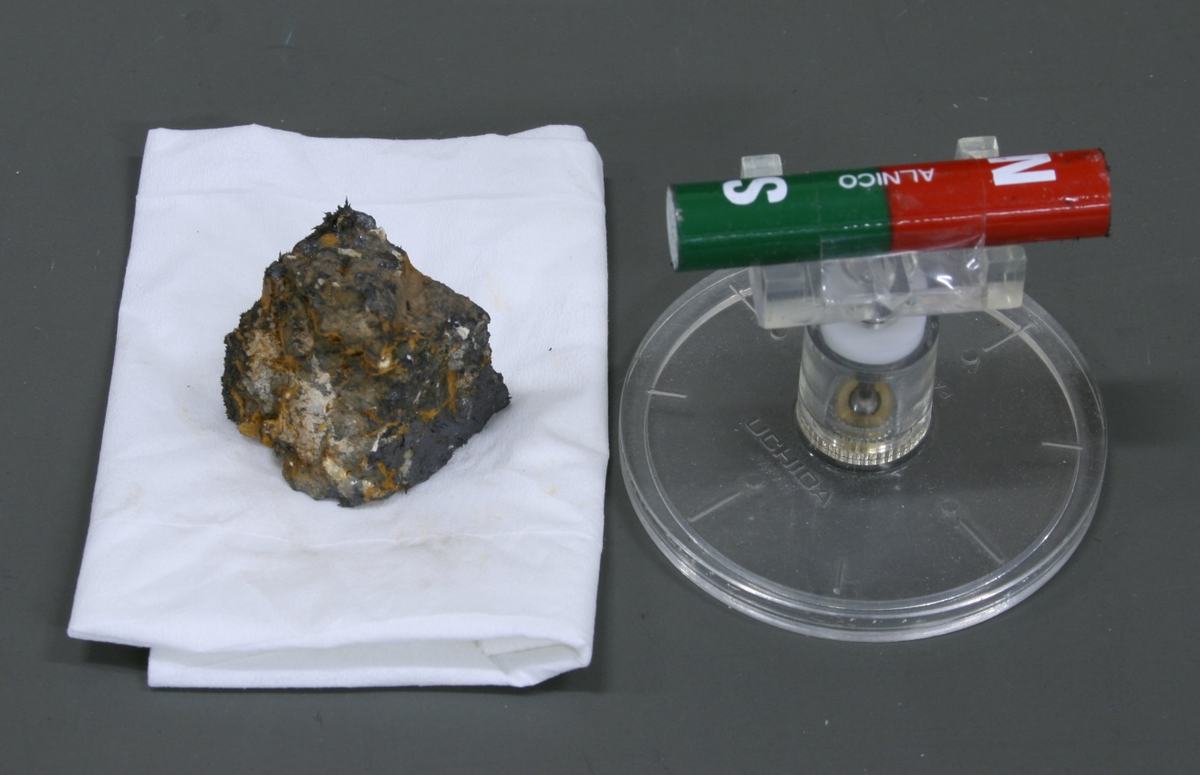 Lodestone on white cloth with ALNICO bar magnet rotated to opposite orientation (green S on left, red N on right) on pivot stand