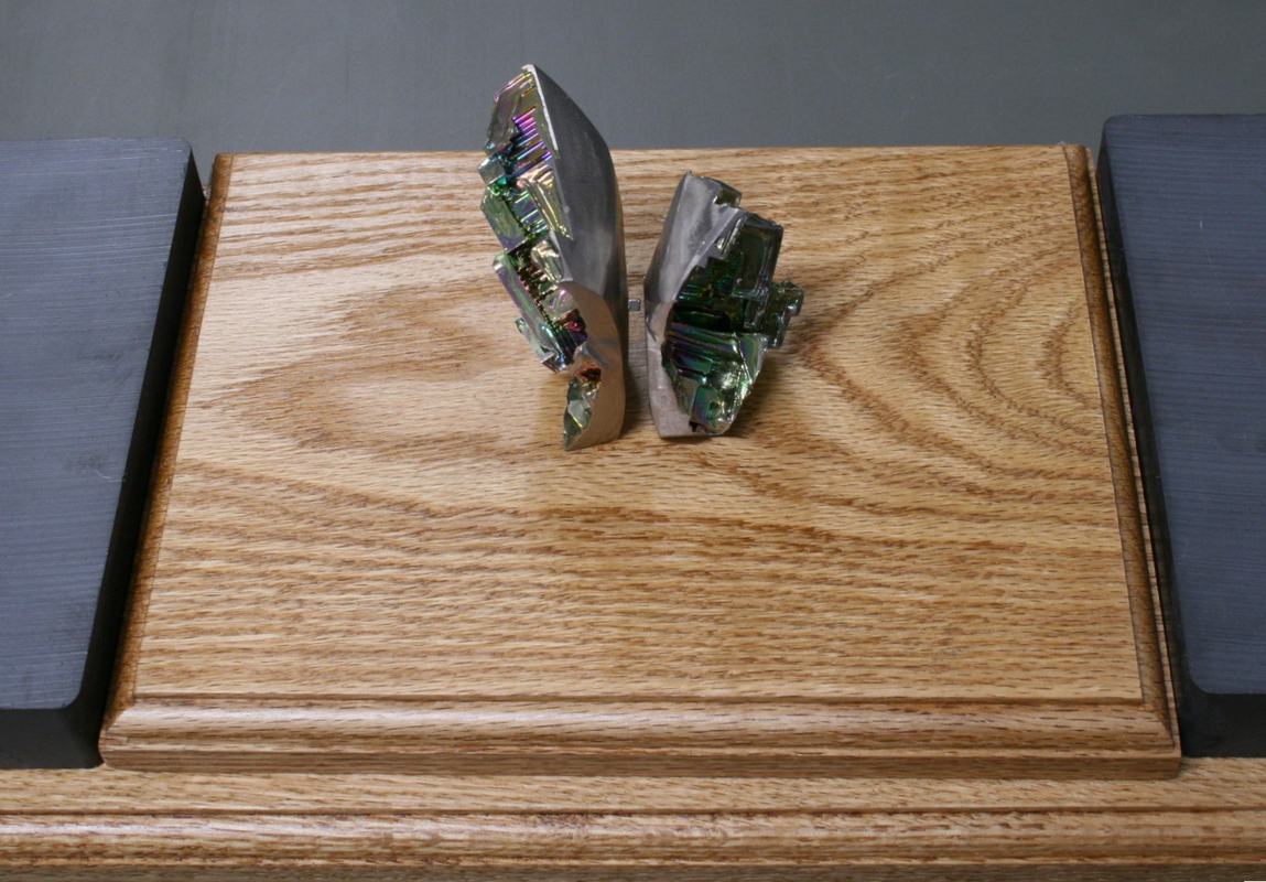 Two bismuth crystal pieces standing upright on a wooden platform, separated by a few centimeters