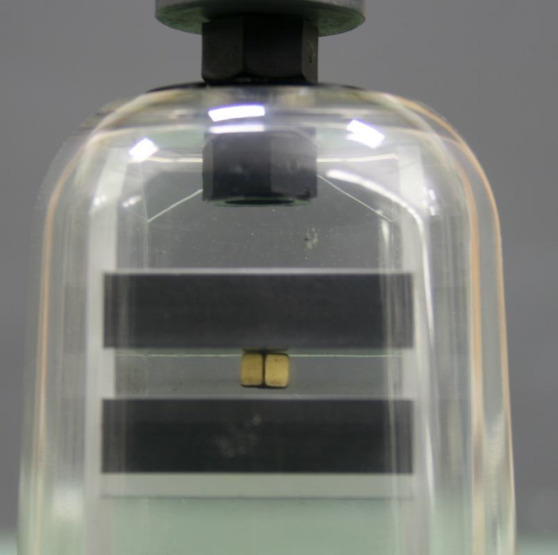 Glass jar with dark lid containing two dark pyrolytic carbon slabs separated vertically, with small gold-colored magnets visible between them and a ceramic magnet mounted at the top