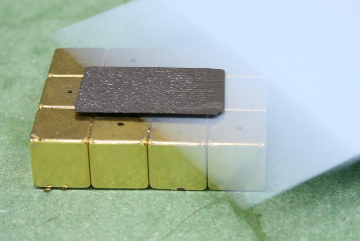 Dark gray rectangular graphite sheet on a 3x4 array of gold and silver cubic magnets on a green surface