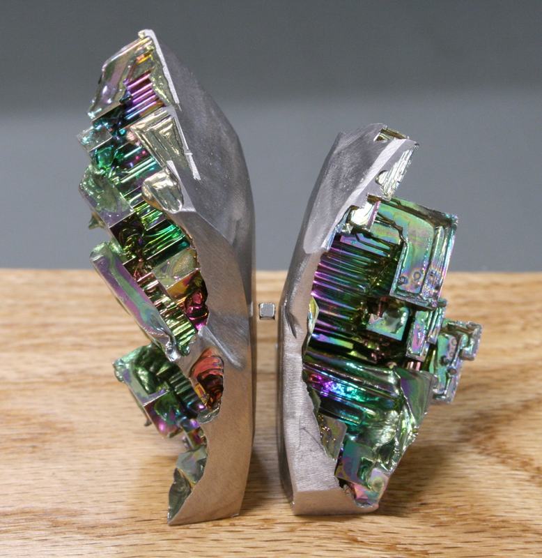 Two bismuth crystal pieces with stepped, geometric surfaces showing rainbow-colored oxidation patterns
