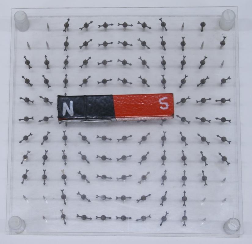 Same needle array with a bar magnet (black N, red S) placed across the center, with nearly all needles now aligned along the field direction