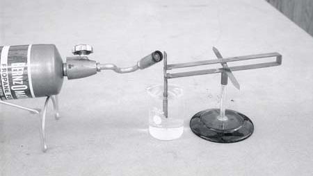 Bernzomatic propane torch on stand heating a copper-constantan thermocouple junction, with compass needle on stand nearby and small beaker of ice water