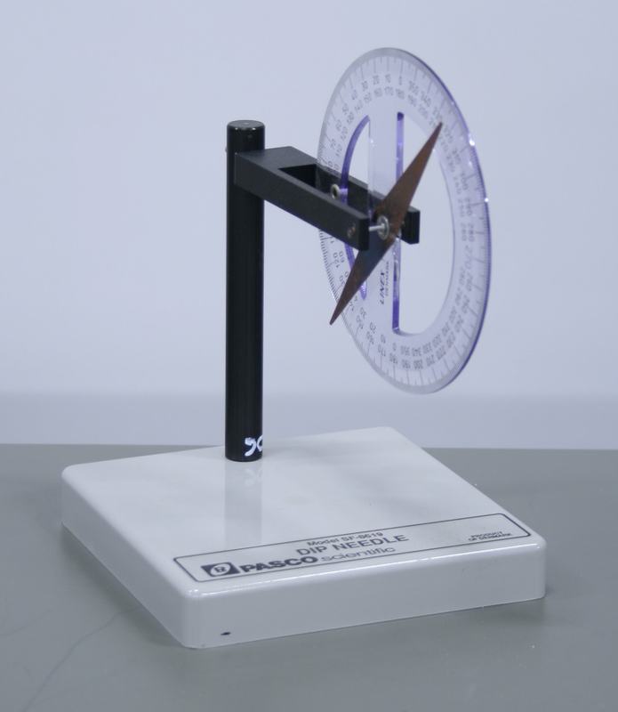 PASCO Scientific dip needle (Model SF-8619) with white rectangular base, black vertical post and horizontal arm supporting a transparent circular protractor with copper-colored magnetized needle