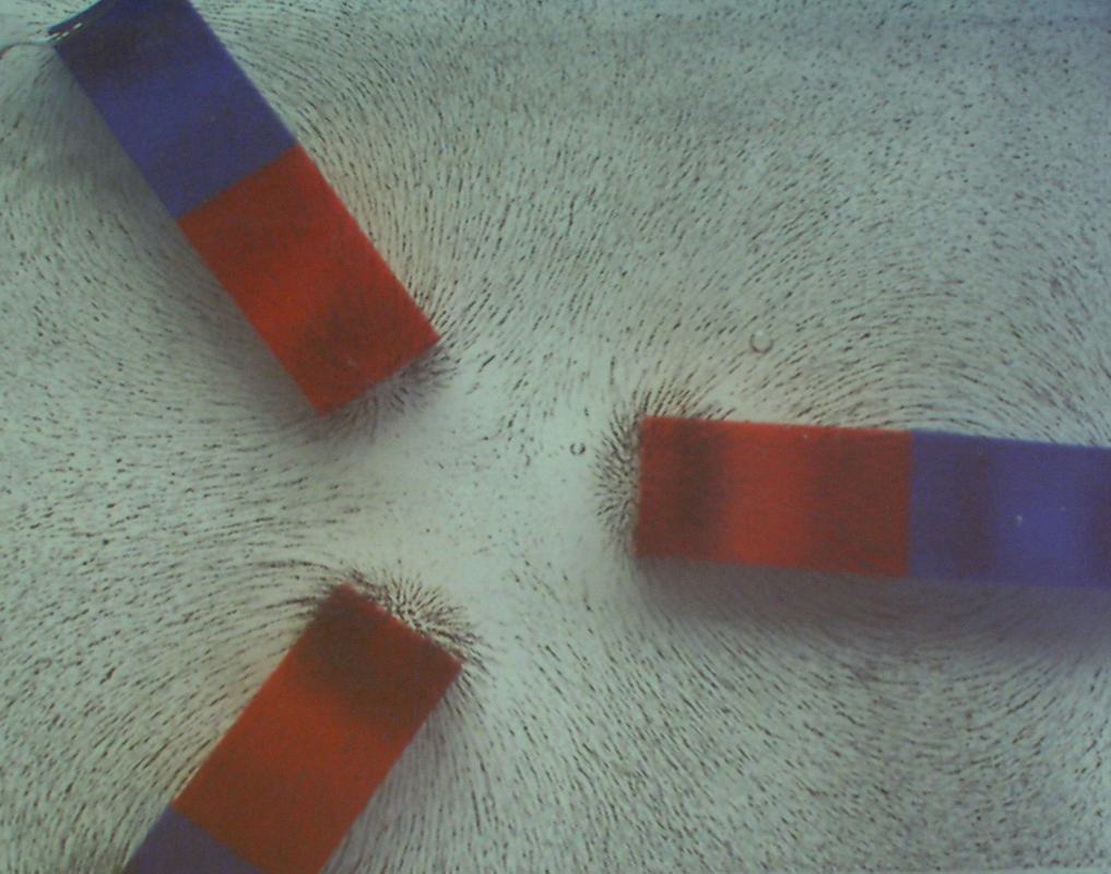 Two bar magnets positioned at different angles showing asymmetric iron filing patterns and field line interactions