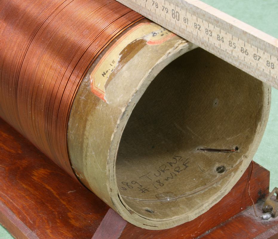 End view of solenoid with a ruler for scale, showing handwritten turn count and wire gauge markings inside the core