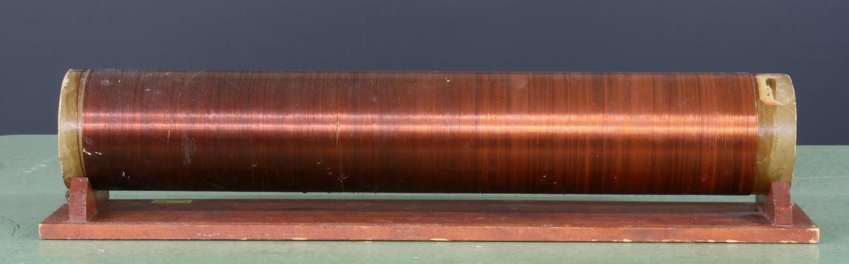 Long copper-wire solenoid wound on a cardboard tube, mounted horizontally on a wooden base
