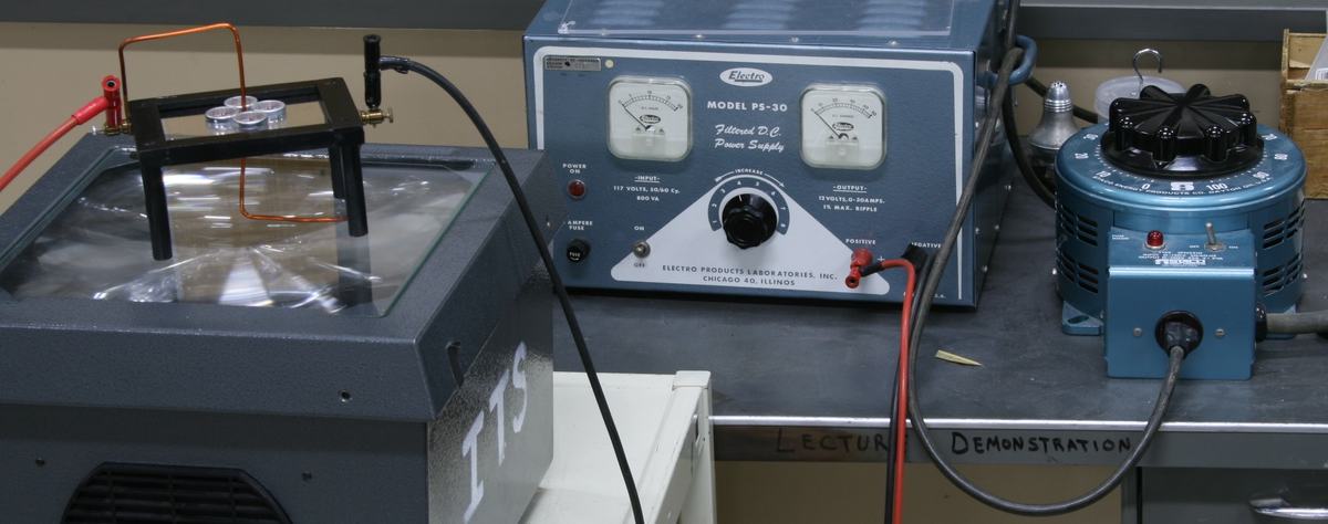 Full bench setup: conductor table on overhead projector at left, Electro PS-30 filtered DC power supply in center, blue Variac variable transformer at right, connected with banana cables