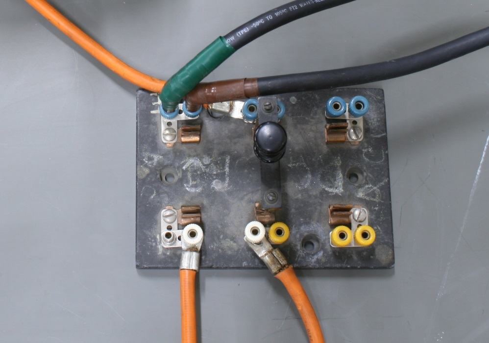 Overhead view of switch junction box showing orange, green, and brown wires connected to brass terminals with yellow identification rings on bottom posts, demonstrating alternate wiring configuration