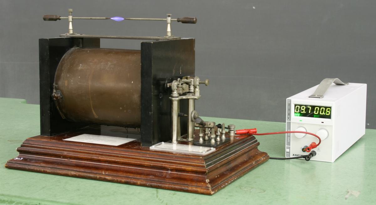 Ruhmkorff induction coil on wooden base with large cylindrical secondary coil between black metal supports, mechanical vibrator assembly at right, discharge terminals on top showing small blue spark, and Xantrex DC power supply reading approximately 9.7 V and 0.8 A