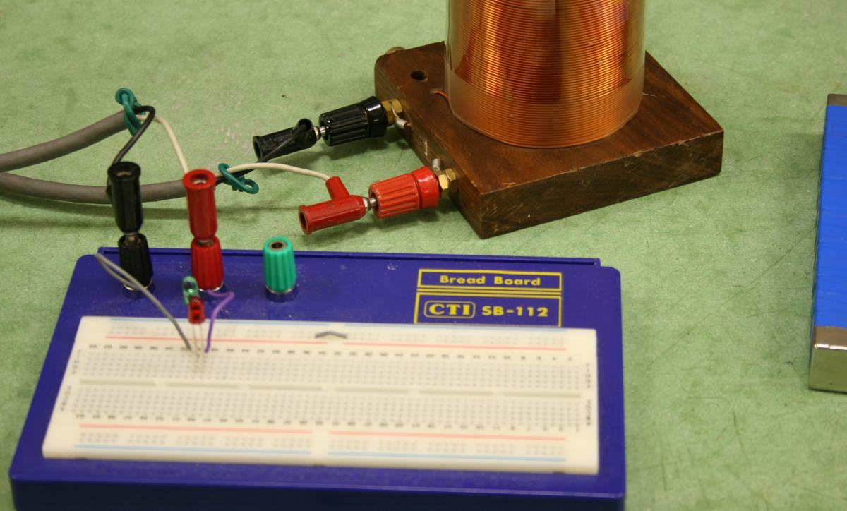 Close-up of CTI SB-112 breadboard with red, green, and black binding posts, two LEDs inserted in opposite orientations, connected to the coil via banana plug leads
