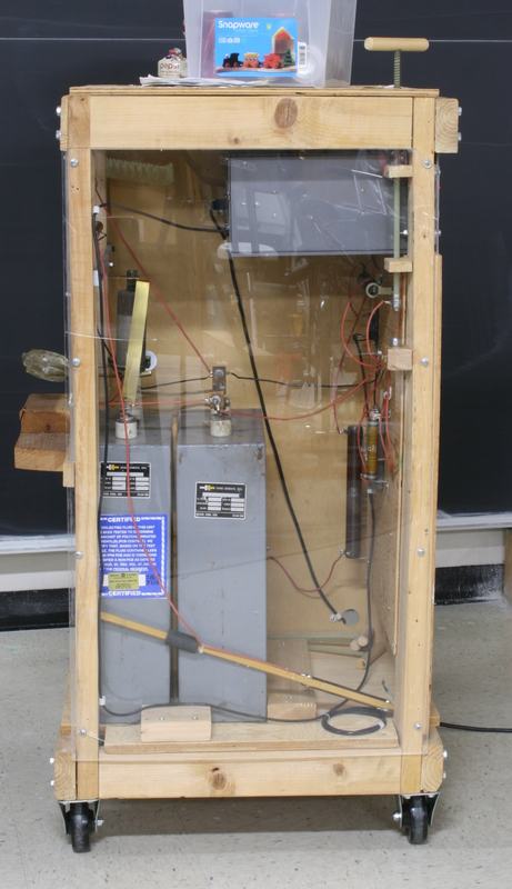 Rear view through acrylic panel showing two large capacitors, Ignitron tube, wiring, bleed resistors, and safety labels