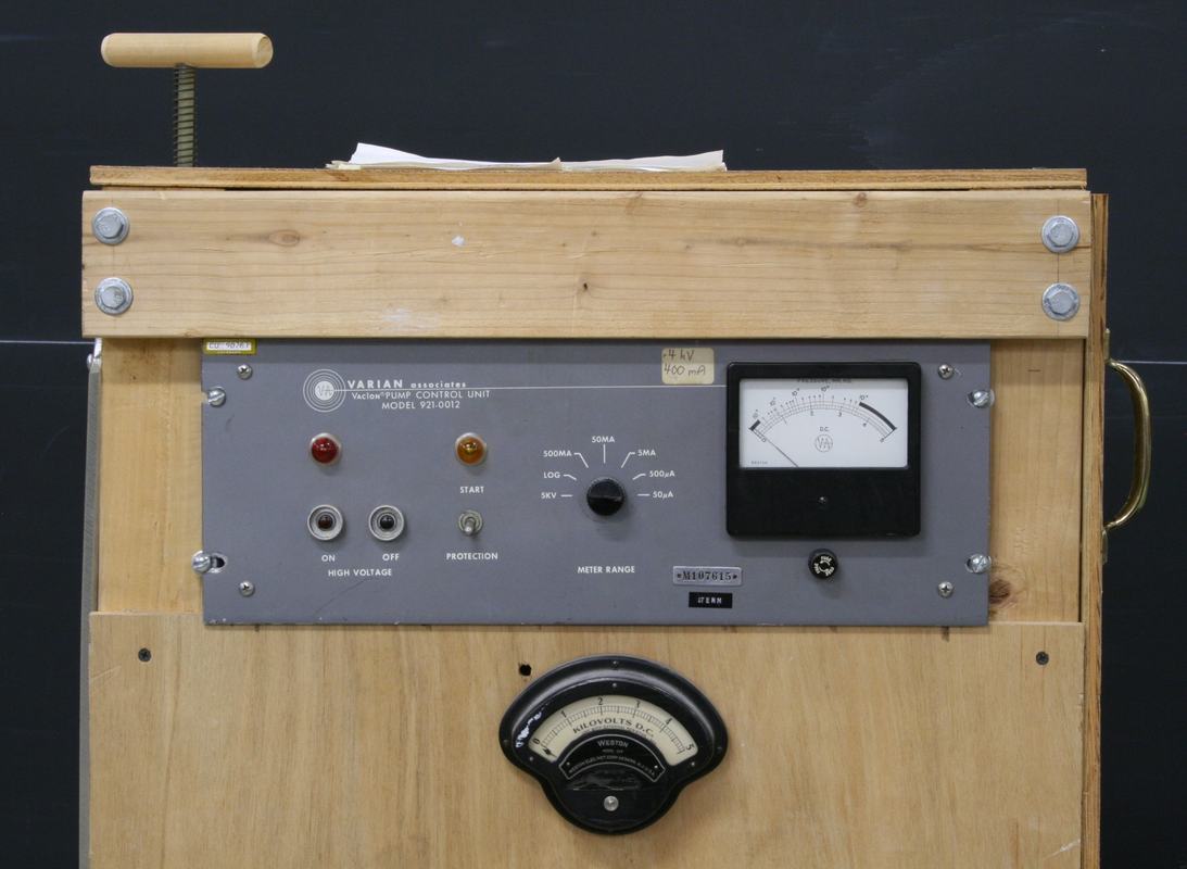 Control panel with Varian Associates power supply, on/off buttons, indicator lights, analog voltage meter, and firing plunger visible at top