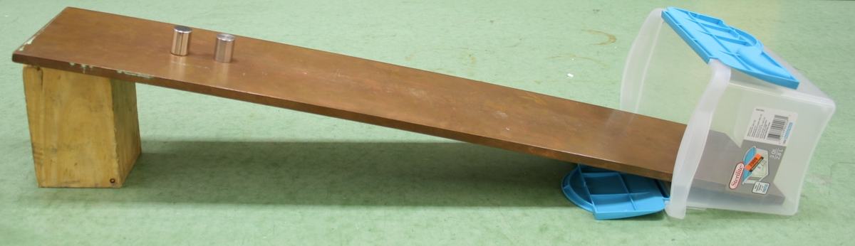 Copper plank inclined on a wooden block, with a cylindrical magnet and stainless steel cylinder at the top and a clear plastic catch box at the bottom