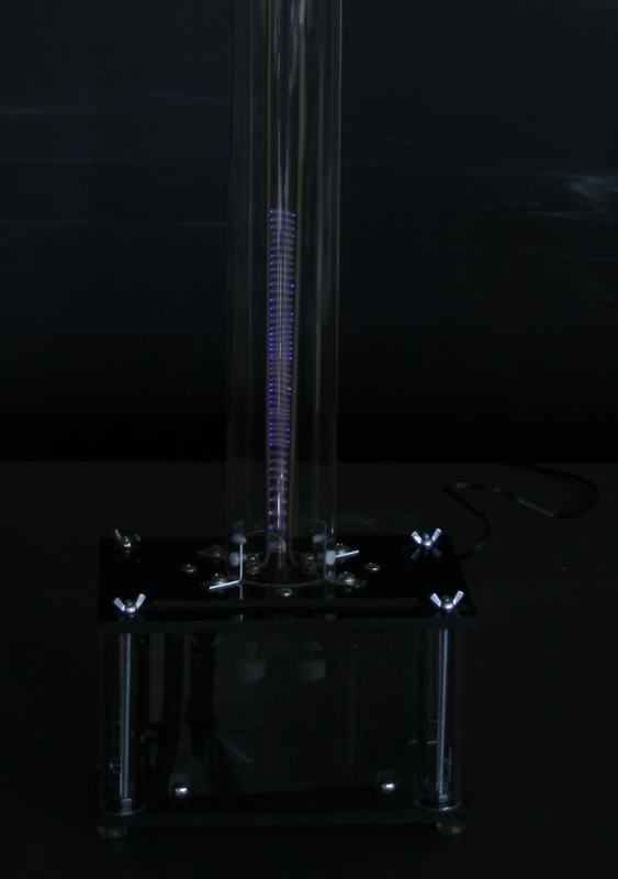 Close-up of Jacob's ladder base in darkened room showing purple-blue arc discharge between the rods inside the glass tube