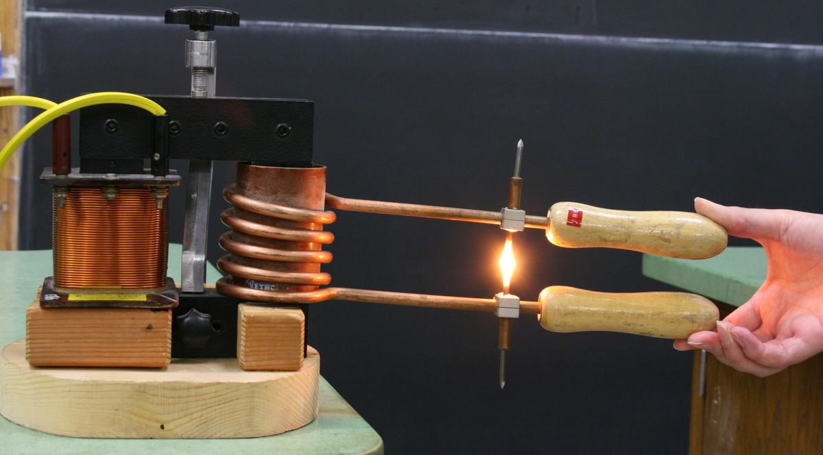 Nail heads held in contact glowing orange-hot from resistive heating, with the demountable transformer visible in the background