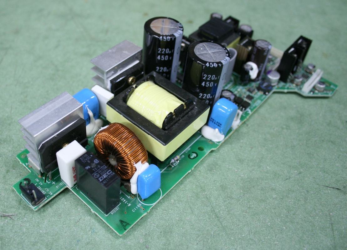 Power supply circuit board from LCD projector showing electrolytic capacitors (220μF 450V), yellow-taped transformer, toroidal inductor, aluminum heatsinks, and blue film capacitors