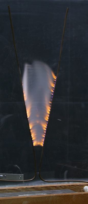 Long-exposure photo of the larger Jacob's ladder showing multiple arcs climbing between V-shaped rods with orange and white plasma, no shield