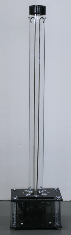 Jacob's ladder with two metal rods inside a tall cylindrical glass tube, mounted on a black acrylic platform over a clear box housing the transformer
