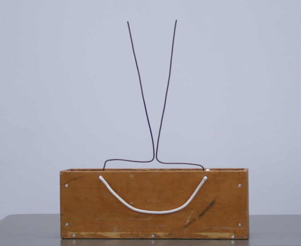 Rear view of the larger Jacob's ladder showing two rods in V-shape mounted on a wooden box containing the transformer, with white power cord