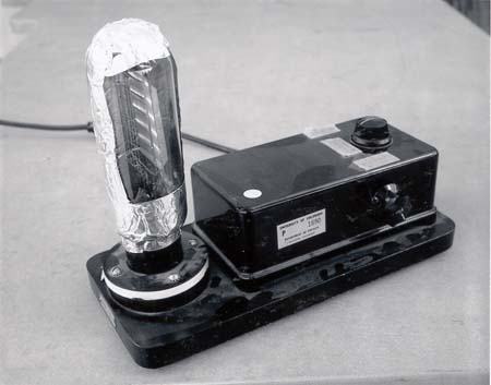 Demonstration triode: large glass vacuum tube mounted vertically on a black base with control knobs for filament, plate, and grid voltages