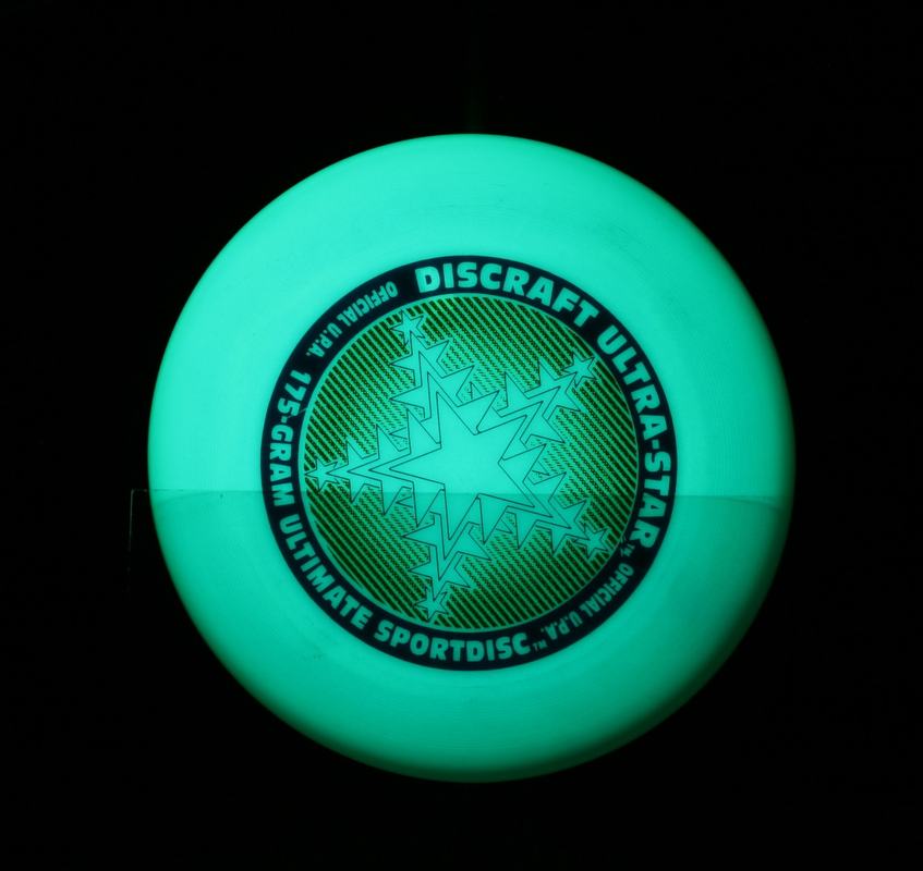Phosphorescent Discraft Ultra-Star disc glowing uniformly green under direct UV illumination