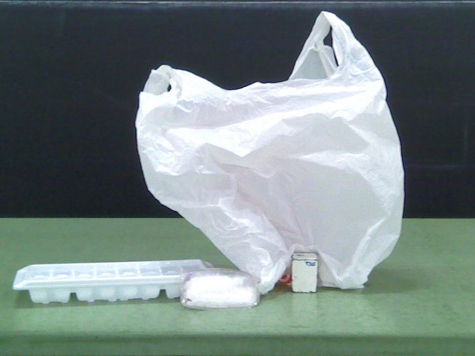 Demo accessories on green bench: white plastic grocery bag, ice cube tray, reusable sodium acetate heat pack, and small white box