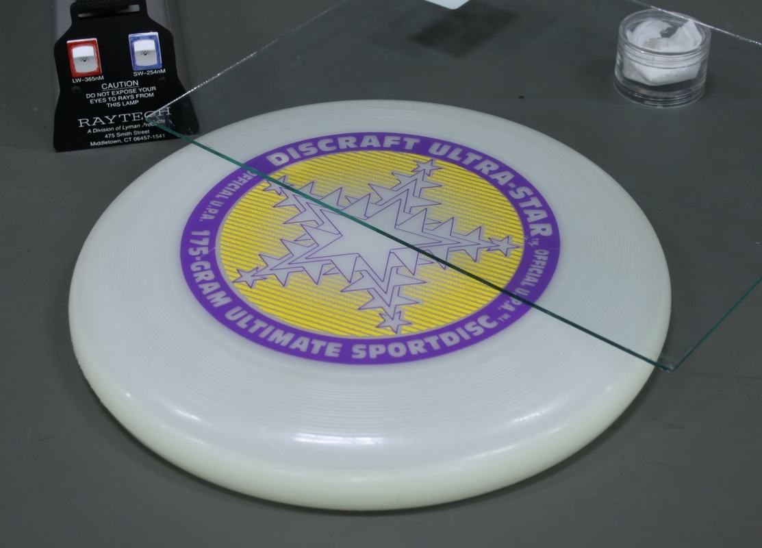 Setup overview: white disc with glass pane leaning against it, Raytech dual-wavelength UV lamp with red (longwave) and blue (shortwave) switches, and plastic phosphor container