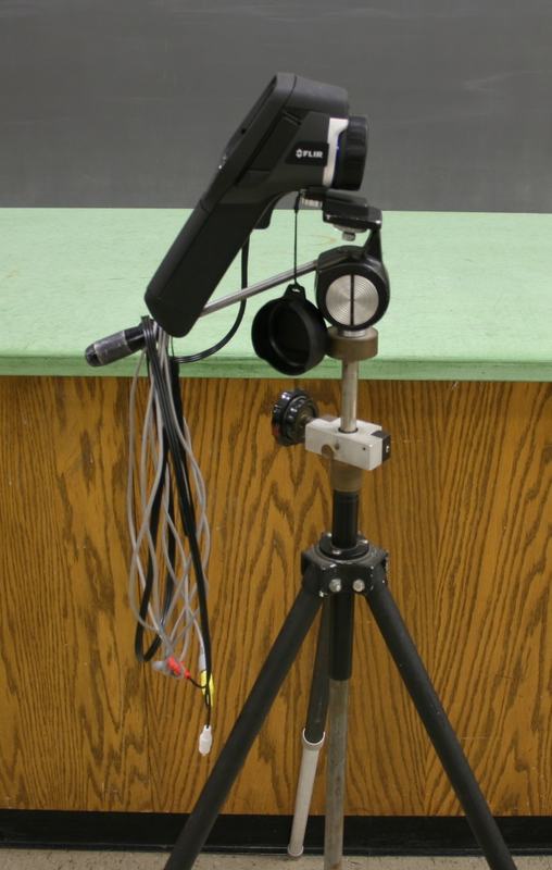 FLIR handheld thermal camera mounted on a tripod via custom bracket, with HDMI and power cables, next to a lab bench