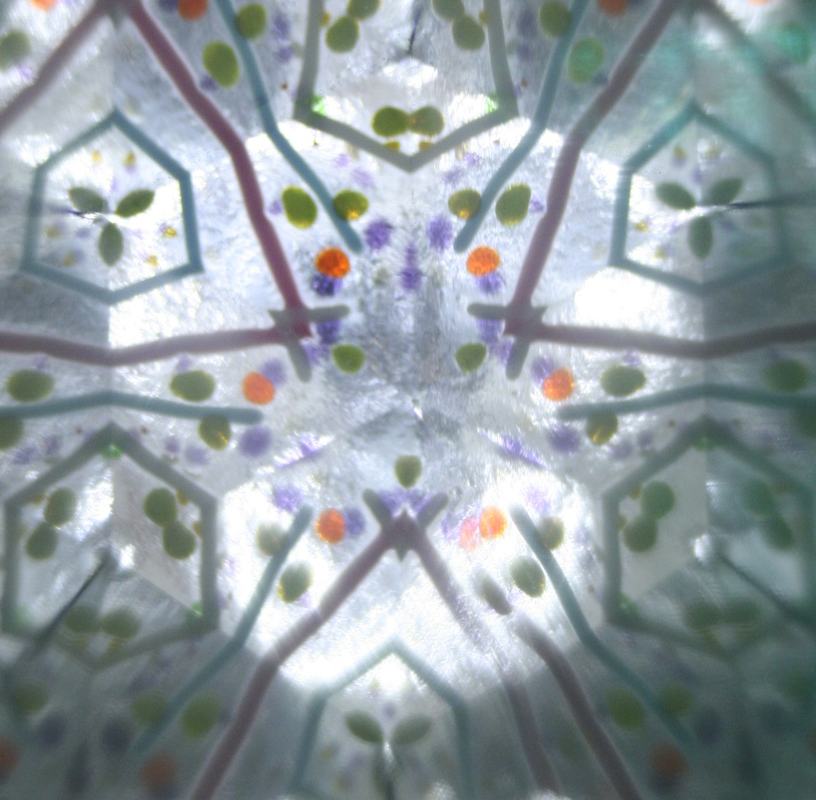 View through a student kaleidoscope showing a six-fold symmetric pattern of orange, green, and purple colored beads with geometric line structures