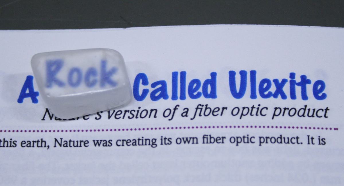 Translucent ulexite stone on printed text reading 'A Rock Called Ulexite' with word 'Rock' visible through the crystal