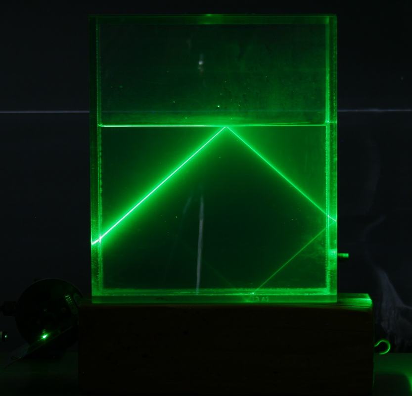 Green laser beam near the critical angle with a bright symmetric V-pattern reflected beam in the water and a dim refracted beam still visible exiting the tank