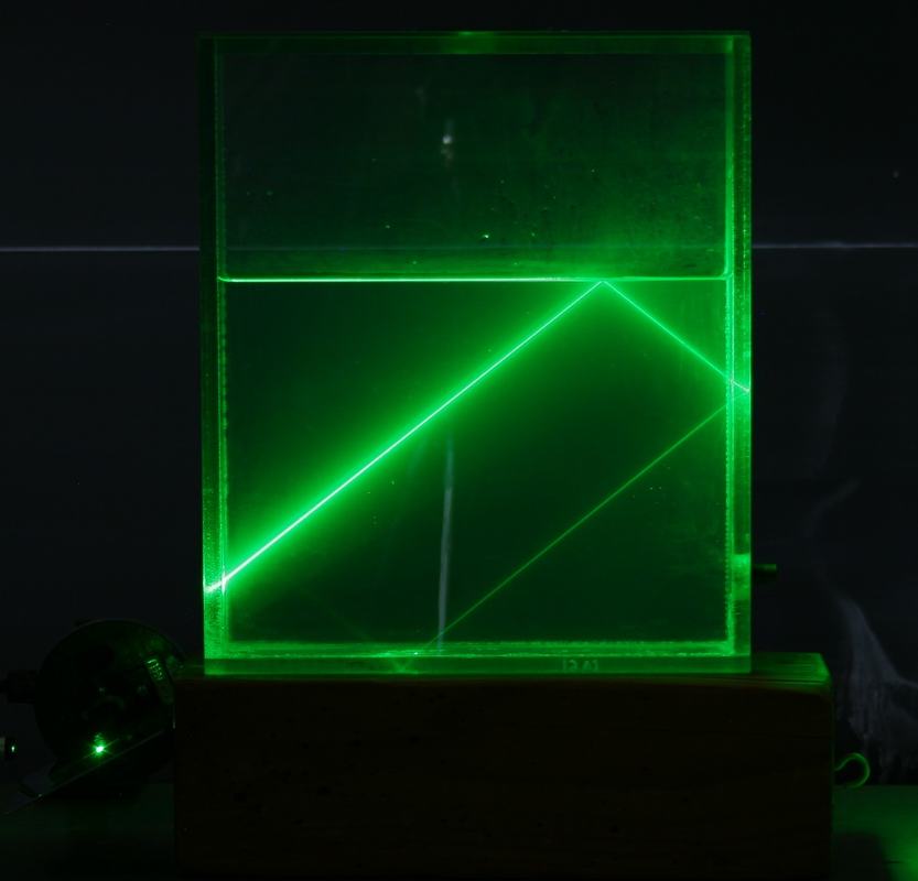 Green laser beam at or beyond the critical angle showing total internal reflection with a bright V-shaped reflected beam in the water and minimal transmission above the surface