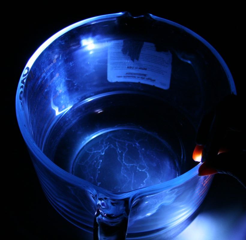 Overhead view into a glass measuring cup with blue light confined within the glass rim, a product label visible inside