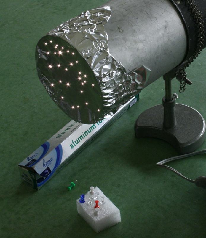 Close-up of cylindrical lamp tube with aluminum foil over the open end, showing many small pinholes glowing with light from the bulb inside