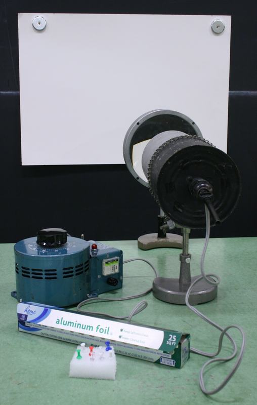 Full apparatus: teal variac, lamp holder with aluminum tube on stand, white poster board magneted to blackboard, aluminum foil box and push pins in styrofoam block