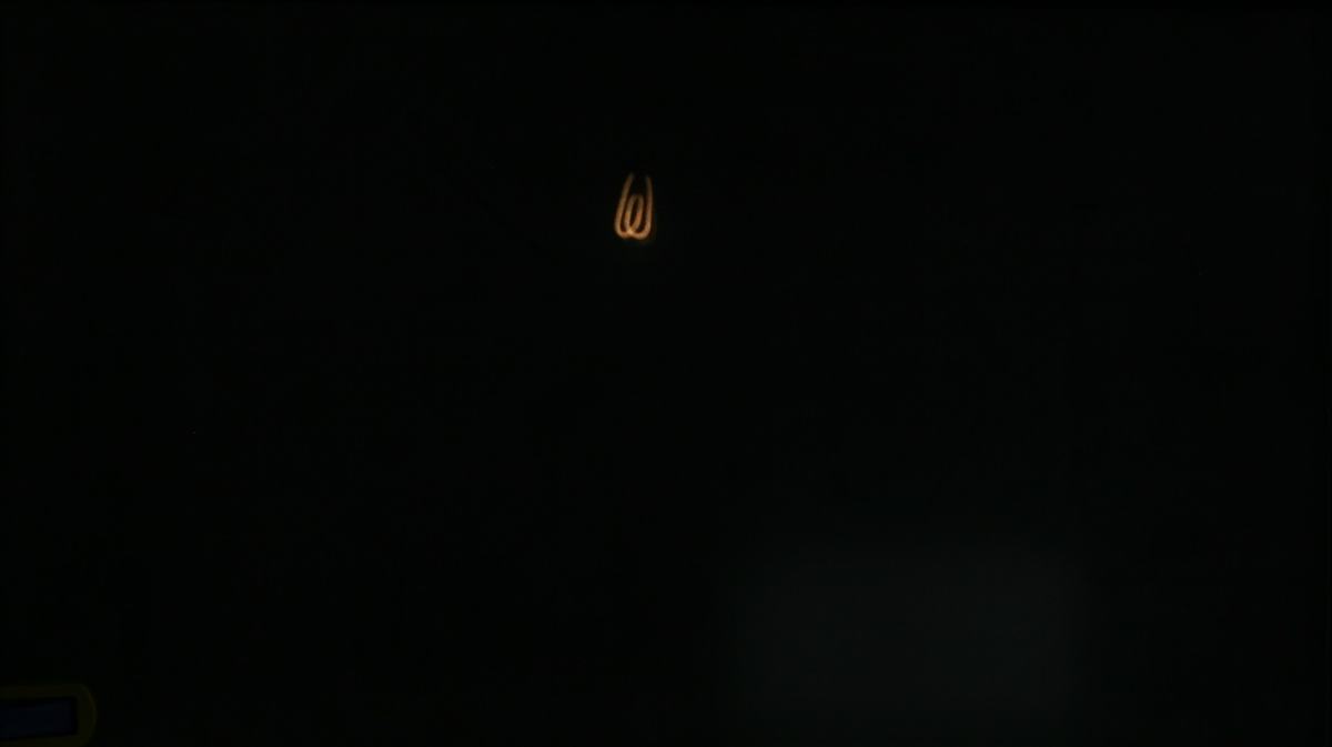Glowing orange coiled filament image projected through pinhole onto dark screen, showing the inverted filament structure of the incandescent bulb