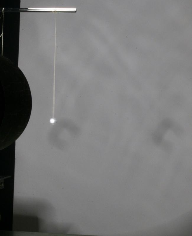 Single pith ball on a thread near the lamp, with filament-shaped shadow patterns visible on the wall behind