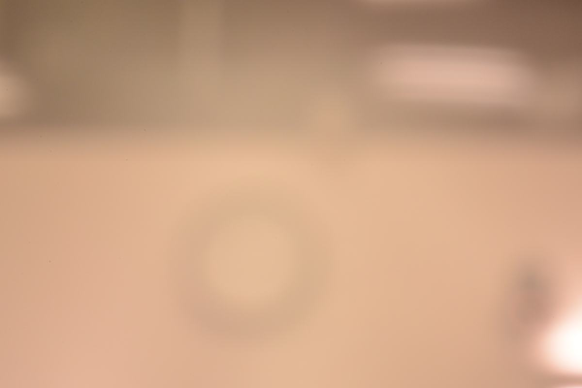 Very blurry, bright photograph of a lecture hall wall clock taken through the largest pinhole; clock outline barely visible through heavy geometric blur