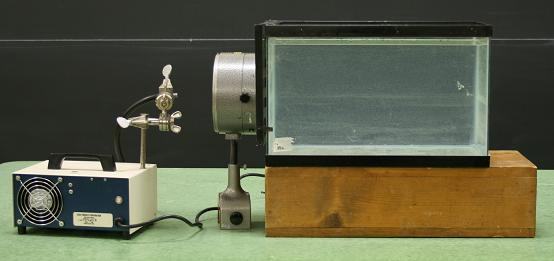Setup: fiber optic lamp and power supply on left, condenser on ring stand in center, water-filled aquarium on wooden block on right