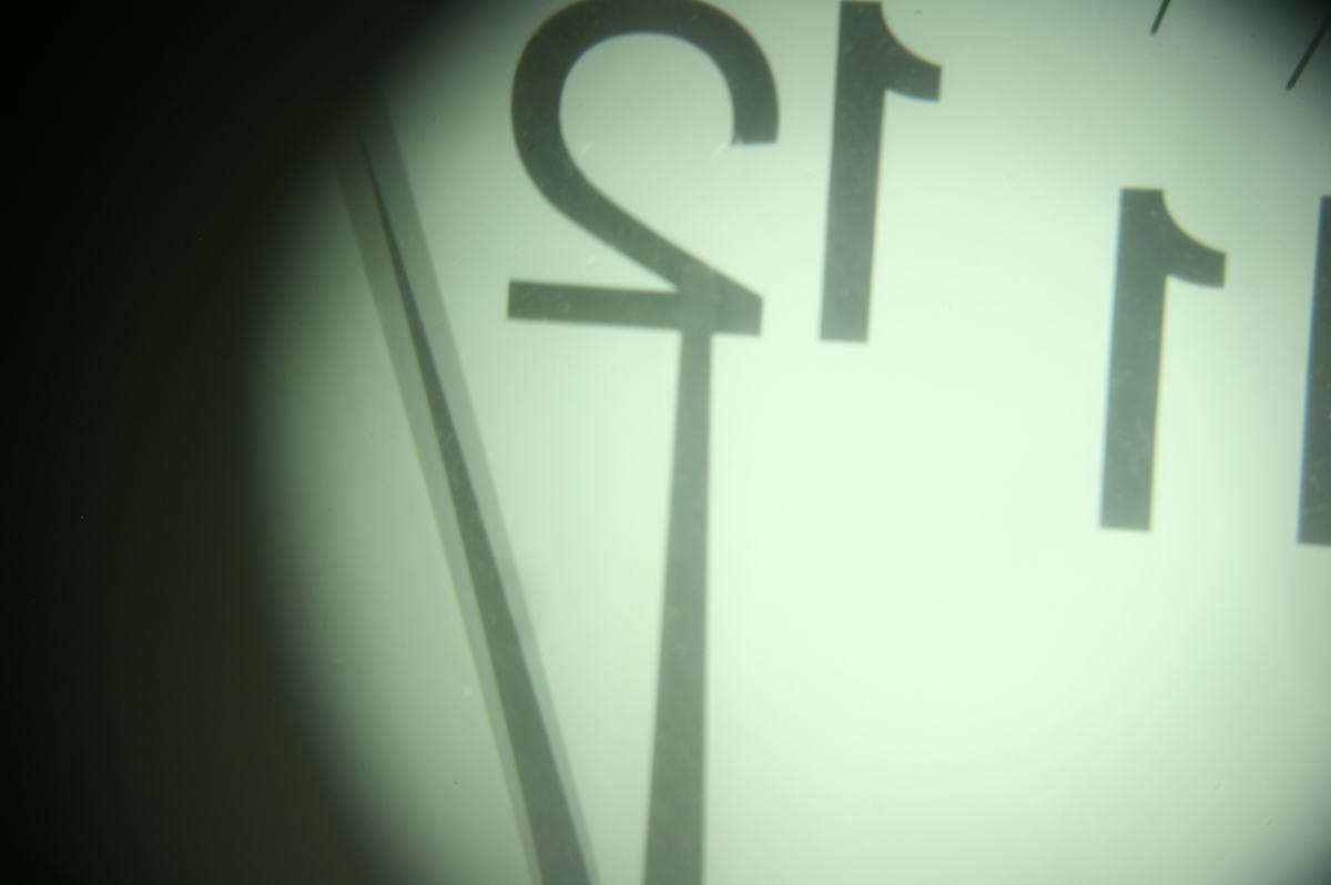 Inverted and magnified view of a clock face through the telescope eyepiece, showing the numbers 12 and 1 upside-down