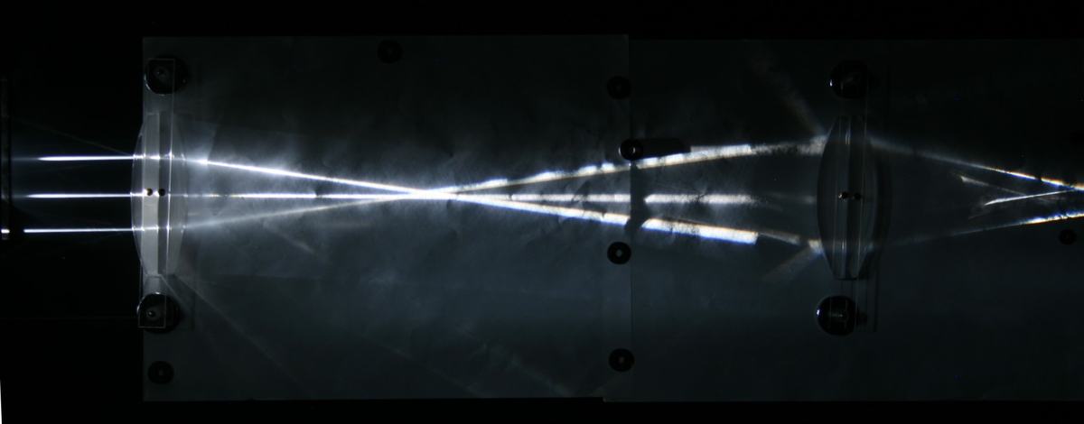 Close-up of two lenses on the magnetic board with rays converging to a focal point between them and showing visible chromatic dispersion through the second lens