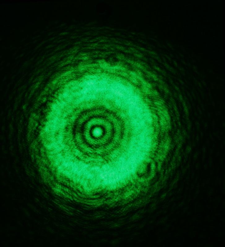 Green Fresnel diffraction pattern with fewer visible rings and slightly asymmetric ring structure, bright Poisson spot still visible at center