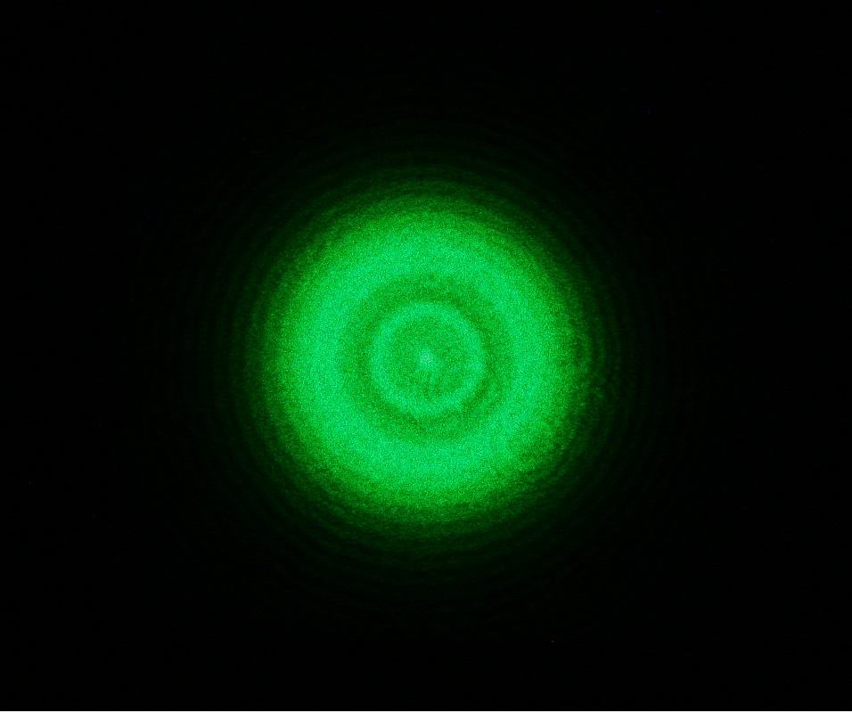 Concentric circular diffraction rings in green laser light on dark background from pinhole aperture