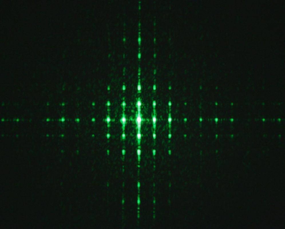Green laser diffraction pattern with cross-shaped symmetry showing bright central core and regular horizontal and vertical arrays of spots