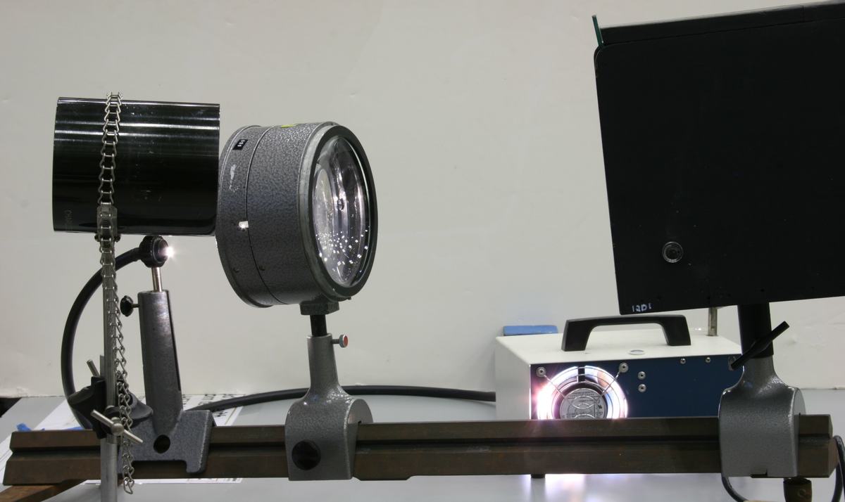 Side view of optical rail showing Beseler projection lens on left, fiber optic illuminator with blue housing in center, and soap film box on right