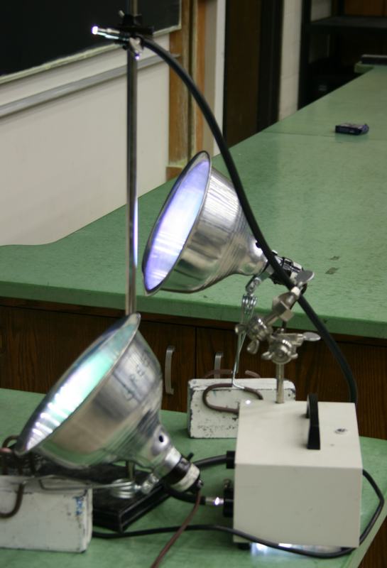 Two clamp-style floodlights with reflector cones and a flexible cable lamp mounted on a lab bench