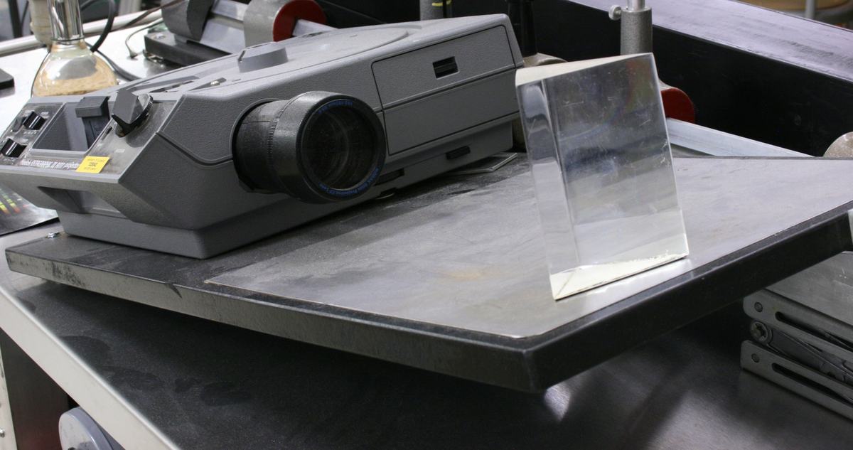 Close-up of Kodak slide projector and equilateral plexiglass prism on metal optical bench platform