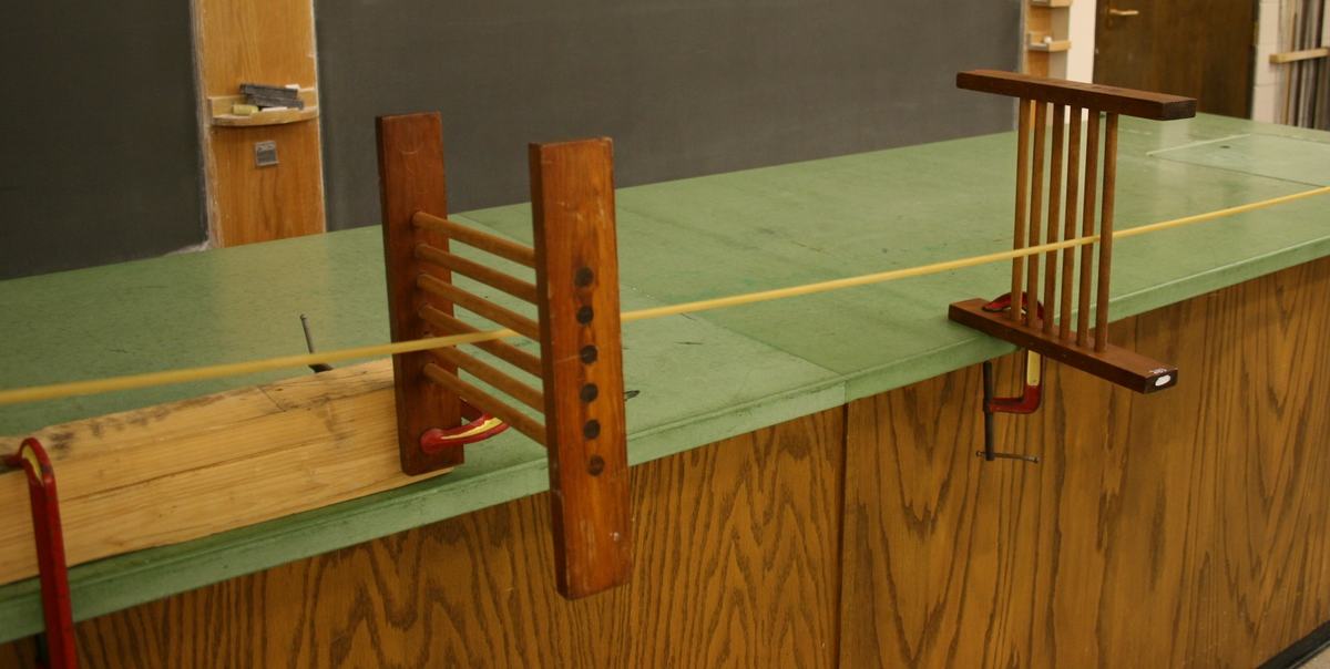 Two wooden polarization grids clamped to a green-topped lecture bench with yellow rubber tube threaded through — one grid has horizontal bars, the other has vertical bars