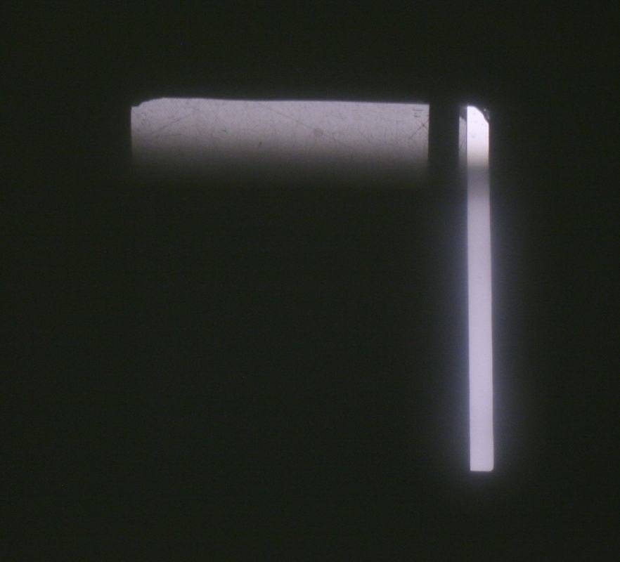 Nearly dark projected screen with only a small bright strip visible at the upper right, showing crossed polarizers blocking almost all light